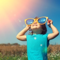 Little girl smiling and holding sunglasses to her face