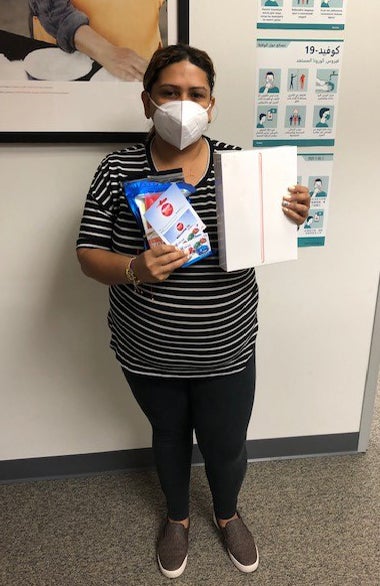 Connecting Communities Program participant, Angelica - wearing her safety mask, holding some supplies given to her by our program (including an iPad)