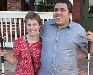 We are standing outside the restaurant. I’m wearing a sundress and he’s wearing a dress shirt with dress pants and dress shoes. We are standing side-by-side with an arm around each other and smiling. It was taken after dinner for our two year anniversary.