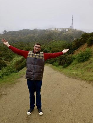 Scott Klumb stands with his arms open in front of the Hollywood sign