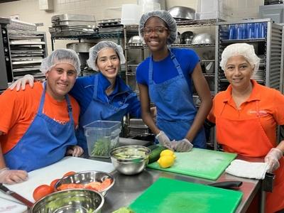 A group of people wearing aprons pose around a table with prepped food