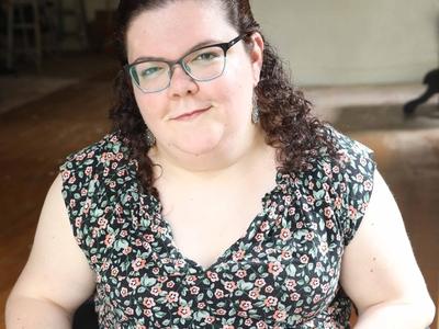 Emily Ladau smiling in a floral blouse and glasses