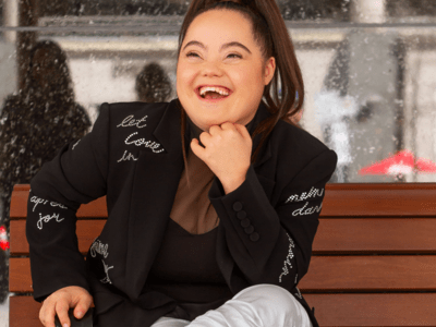 Madison Tevlin laughing on a bench with a jacket that has the words "let love win" on it