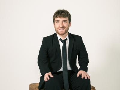 Photo of Nic Novicki in a suit, sitting on a crate