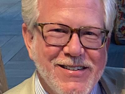 Ted Thompson in a light-colored suit and brown framed glasses