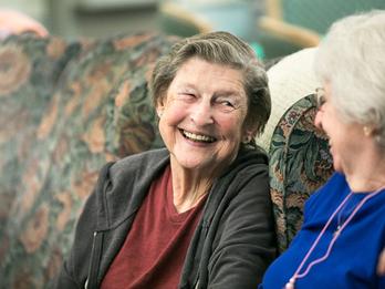 Two older adults smiling at each other while sitting on a couch