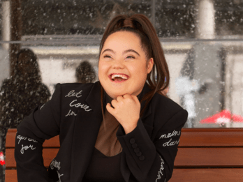 Madison Tevlin laughing on a bench with a jacket that has the words "let love win" on it