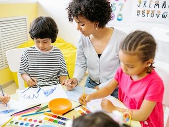 A woman in a classroom teaching two young children