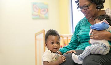 A Easterseals staff member holding a baby and smiling at a toddler