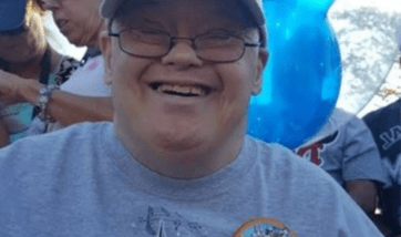 Bill, an adult male, is at an outdoor celebration smiling. He's wearing glasses and a cap. 