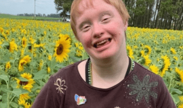 A woman with Down syndrome smiles in a field of sunflowers