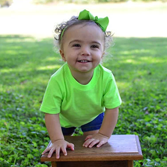 Little girl with green shirt and hair bow smiling